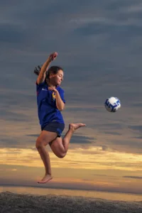 sport féminin, athlète de football féminine à la plage en train d'effectuer un dribble aérien.